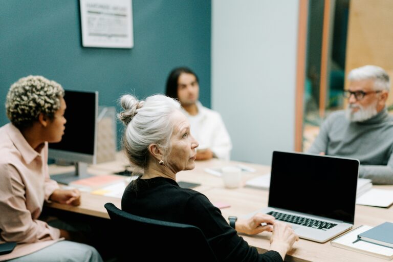 A multicultural team engaged in a meeting around a conference table with laptops.