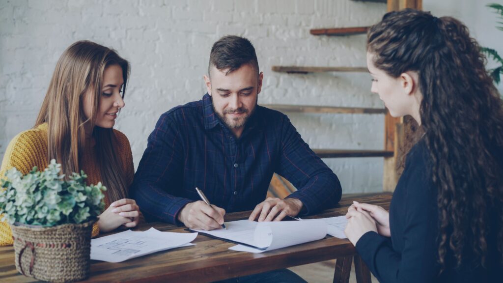 A young couple discussing paperwork with a real estate agent indoors.
